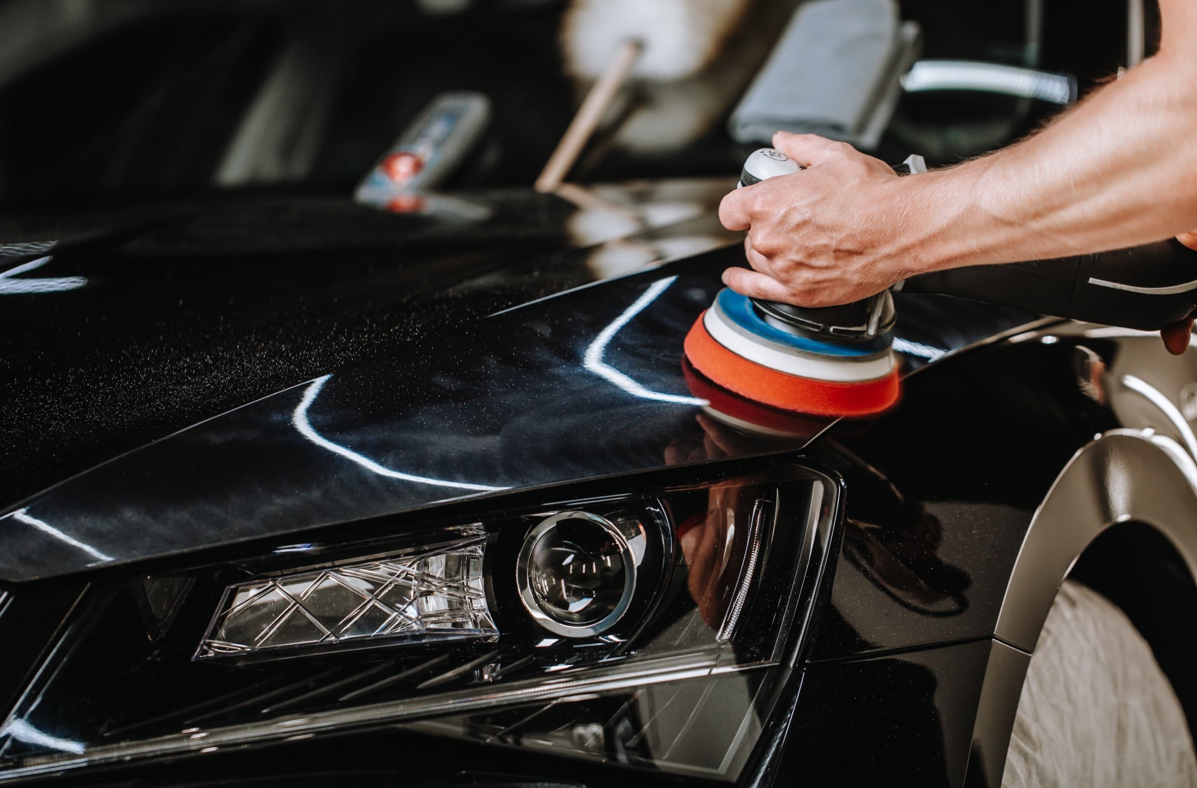 Orbital polisher working a dark painted panel, detailer's hand in frame